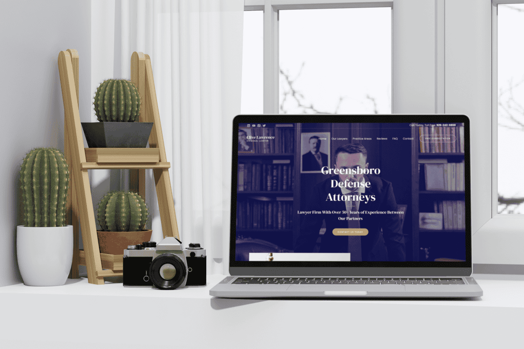 A modern workspace featuring a laptop displaying "Greensboro Defense Attorneys" website, beside cactus plants on a wooden stand and a vintage camera.