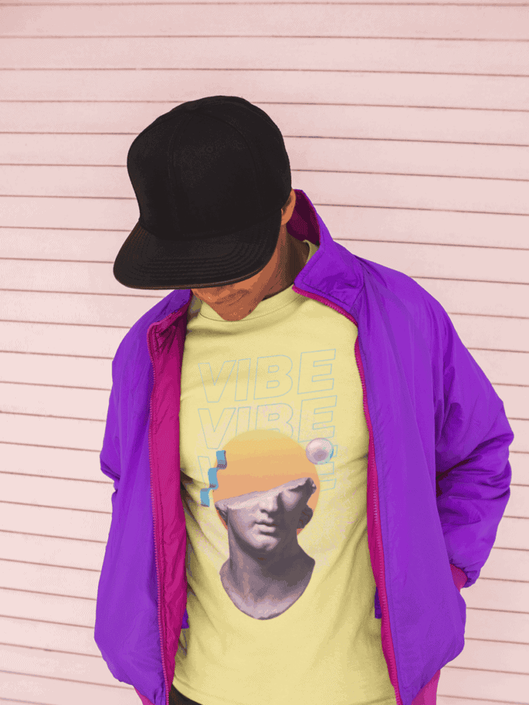 A person in a purple jacket and black cap looks down, wearing a yellow shirt with a graphic of a statue's head and the word "VIBE" against a pink-striped background.